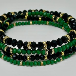 Könnte beinhalten: Ein mehrreihiges Armband mit schwarzen und grünen Perlen. Die Perlen sind mit goldenen Zwischenstücken durchsetzt.