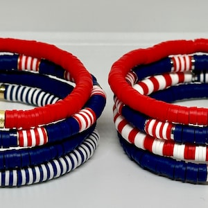 May include: Set of six colorful bracelets with red, white, and blue beads. The bracelets are stacked on top of each other, creating a layered effect.