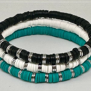 May include: Three stacked bracelets made of black, white, and turquoise ceramic beads. Each bracelet has a silver metal accent between each bead.