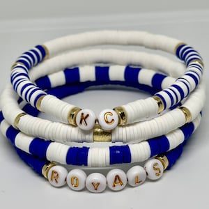 May include: Four stacked bracelets with white and blue striped beads and gold letter beads spelling "ROYALS" and "KC".