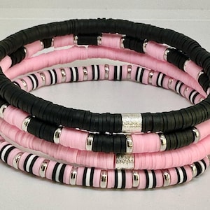 Könnte beinhalten: Ein Set aus vier Armbändern aus rosa und schwarzen Perlen mit silbernen Akzenten. Die Armbänder sind übereinander gestapelt.