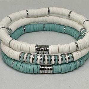 May include: Three stacked bracelets with white and light blue ceramic beads and silver metal accents.