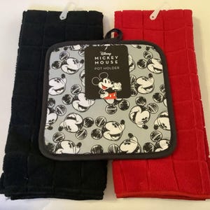 May include: A kitchen set featuring a black and a red dish towel, and a Mickey Mouse pot holder. The pot holder has a gray background with Mickey Mouse faces and the text "Disney Mickey Mouse Pot Holder".