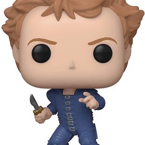May include: A Funko Pop vinyl figure of a character with light skin, brown hair, and black eyes. The figure is wearing a blue jumpsuit and holding a knife with a gold handle. The figure is in a dynamic pose, suggesting action.