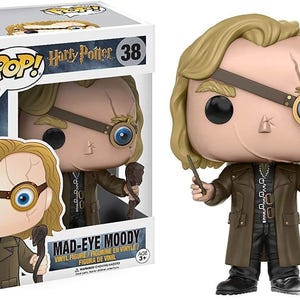 May include: A Funko Pop! vinyl figure of Mad-Eye Moody from the Harry Potter series. The figure has a tan complexion, blonde hair, and a brown coat. It holds a wand and a staff. The box is white with the words "Harry Potter 38".
