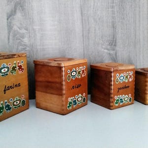 Könnte beinhalten: Vier Holzkisten mit bunten Blumendesigns und Etiketten mit der Aufschrift "farina", "riso", "passione" und "caffe".