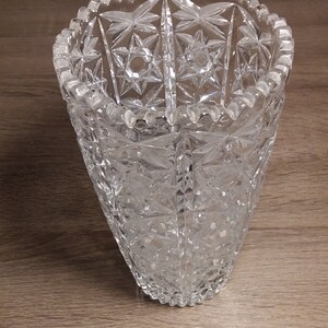 Puede incluir: Un jarrón de vidrio transparente con un diseño de vidrio cortado. El jarrón tiene una boca ancha y una base estrecha.