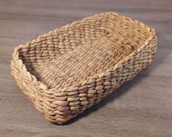 May include: A rectangular woven basket made of natural fibers. The basket has a sturdy, open design with a textured surface and a slightly raised rim. The basket is a light brown color and appears to be handmade.