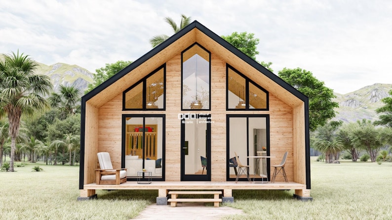 K&ouml;nnte beinhalten: Eine moderne Holzh&uuml;tte mit einem gro&szlig;en, dreieckigen Fenster und einer schwarzen T&uuml;r. Die H&uuml;tte hat eine Holzterrasse und ist von &uuml;ppigem Gr&uuml;n umgeben.