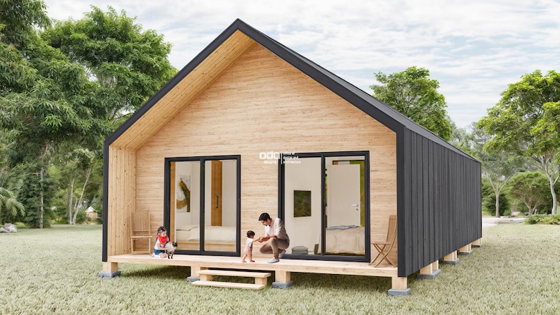 K&ouml;nnte beinhalten: Eine kleine, moderne H&uuml;tte mit einer Holzfassade und einem schwarzen Dach. Die H&uuml;tte hat gro&szlig;e Fenster und eine Terrasse mit einem Gel&auml;nder. Drei Personen stehen auf der Terrasse, darunter zwei Kinder.