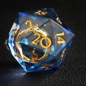 May include: A blue and clear twenty-sided die with gold numbering and accents. The die is made of a transparent material with a blue hue and gold-colored numbers. The number 20 is prominently displayed.