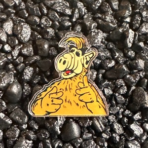 May include: A yellow and brown cartoon character with a large nose and a wide smile. The character is wearing a furry coat and has a surprised expression on its face. The character is a pin or button.
