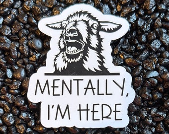 May include: White sticker with a black and white illustration of a sheep with its mouth open. The text "Mentally, I'm Here" is written below the sheep.