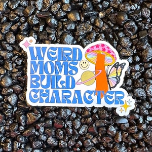 May include: A sticker with blue and white text that reads "Weird Moms Build Character" with a mushroom and butterfly graphic. The sticker is on a black background.