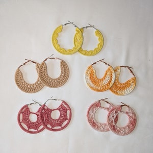 May include: Six pairs of crocheted hoop earrings in various colours, including yellow, orange, pink, and beige. The earrings are all handmade and feature intricate designs.