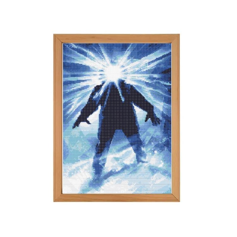 Puede incluir: Una obra de arte de punto de cruz enmarcada que representa una figura con una chaqueta azul de pie en un paisaje nevado con una luz blanca brillante que emana de su cabeza.