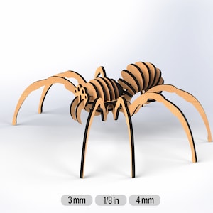 May include: A wooden spider model with black accents. The spider is made of multiple pieces that are assembled together. The spider is about 3 inches tall and 4 inches wide.