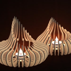 May include: Two wooden candle holders with a geometric design. The holders are shaped like a teardrop and have a small opening at the top for a candle. The candles are lit and glowing.