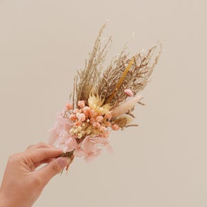 May include: A dried flower bouquet with pink hydrangeas, beige pampas grass, and small pink and white flowers.