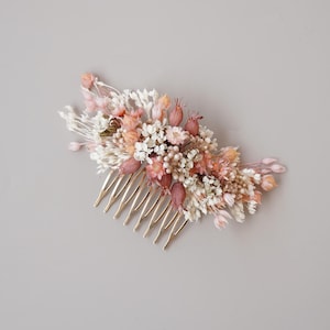 May include: A gold hair comb decorated with dried flowers in shades of pink and white. The flowers are arranged in a cluster and create a delicate and romantic look.
