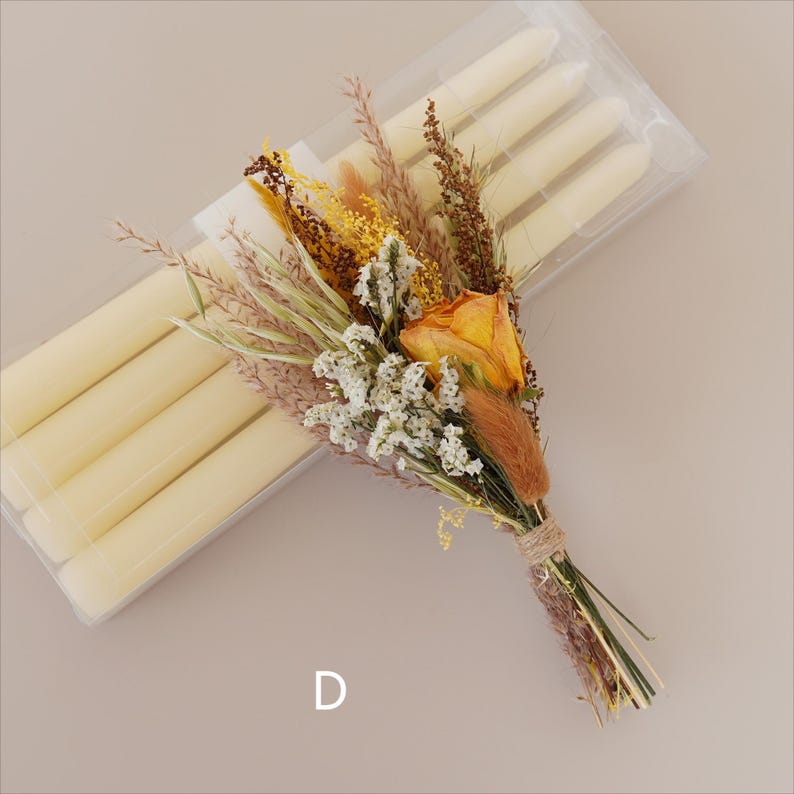 May include: A bouquet of dried flowers in shades of yellow, brown, and white, tied with twine. The bouquet is next to a package of ivory taper candles.