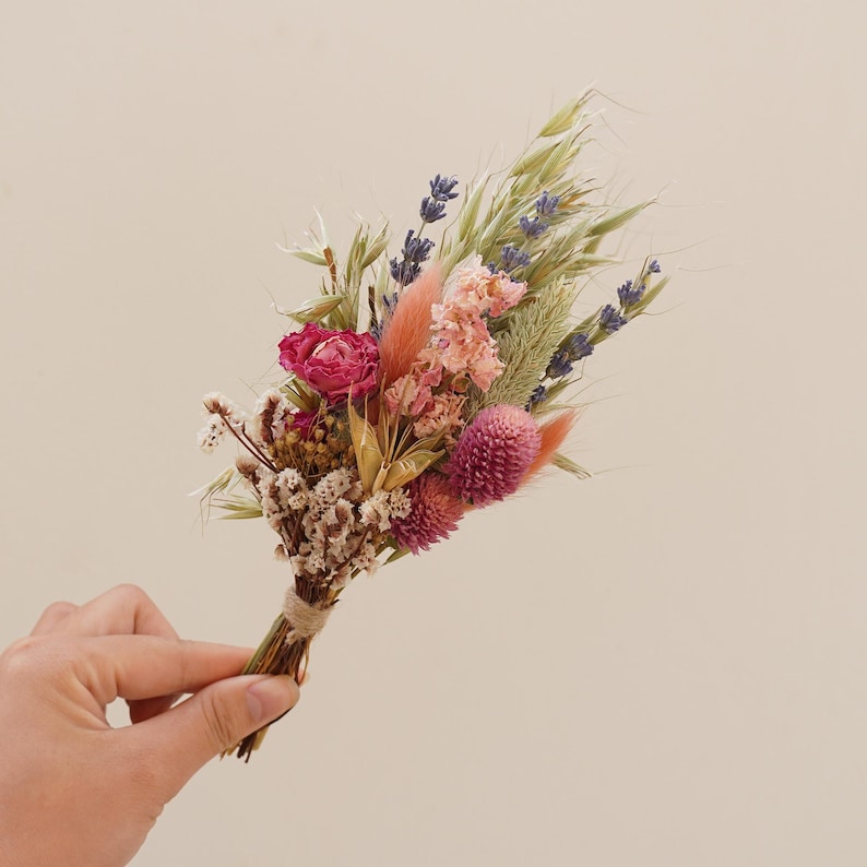 May include: A small bouquet of dried flowers in shades of pink, purple, and green. The bouquet includes lavender, pink and white wildflowers, and dried grasses.