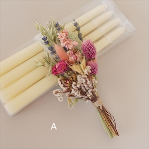 May include: A bouquet of dried flowers in shades of pink, purple, and white, tied with twine. The bouquet is sitting on top of a package of white candles.