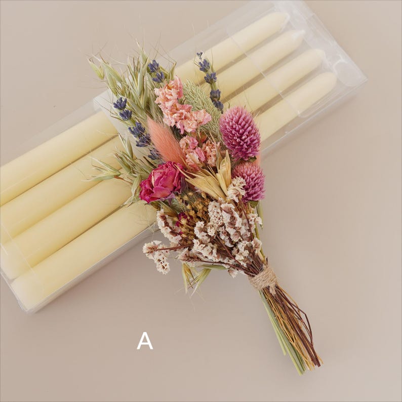May include: A bouquet of dried flowers in shades of pink, purple, and white, tied with twine. The bouquet is sitting on top of a package of white candles.
