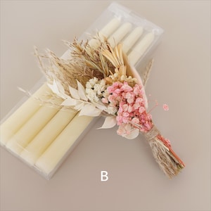 May include: A bouquet of dried flowers in shades of pink, white, and beige, tied with twine. The bouquet is next to a clear plastic package containing four white taper candles.