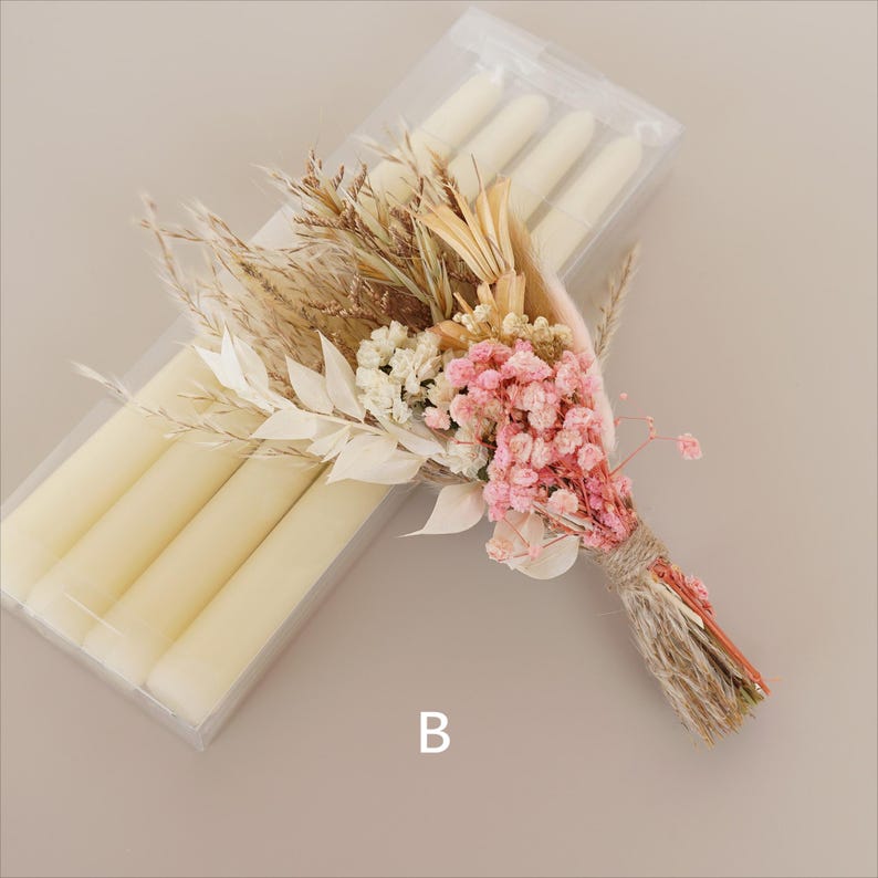 May include: A bouquet of dried flowers in shades of pink, white, and beige, tied with twine. The bouquet is next to a clear plastic package containing four white taper candles.