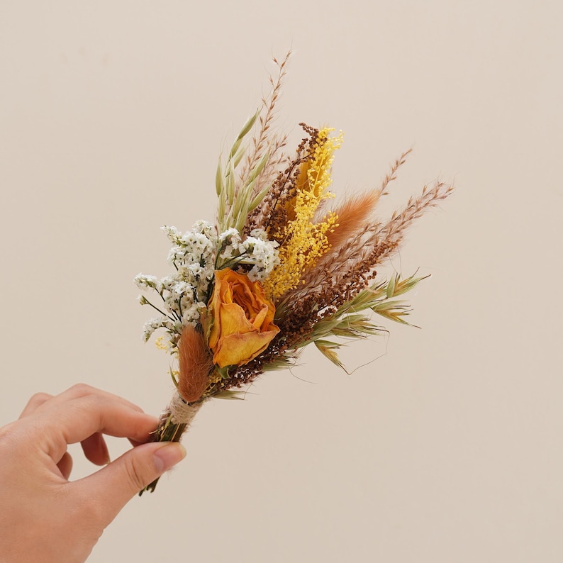 May include: A small bouquet of dried flowers with a single orange rose, white baby's breath, and yellow and brown grasses.