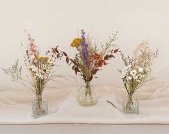 May include: Three glass vases with dried flower arrangements. The vases are clear glass with a textured surface. The flowers are a mix of white, yellow, purple, and red.