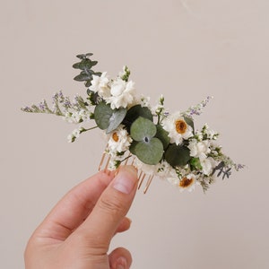May include: A white and green floral hair comb with dried flowers and greenery. The comb is gold and has a delicate design.