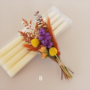May include: A bouquet of dried flowers in shades of orange, yellow, and purple, tied with twine. The bouquet is next to a package of white taper candles.