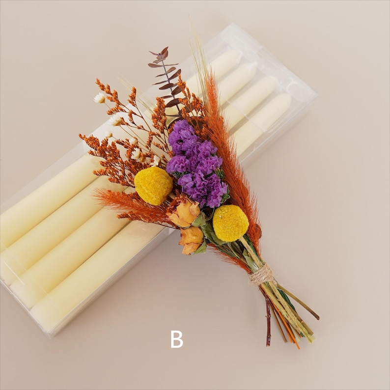 May include: A bouquet of dried flowers in shades of orange, yellow, and purple, tied with twine. The bouquet is next to a package of white taper candles.