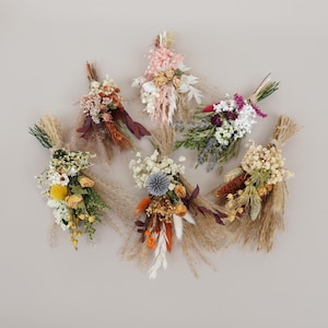 May include: Six small bouquets of dried flowers in various colours, including pink, white, lavender, orange, and yellow. The bouquets are tied with twine and feature dried grasses and other natural elements.