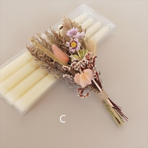 May include: A bouquet of dried flowers in shades of pink, brown, and white, tied with twine. The bouquet is next to a package of white taper candles.