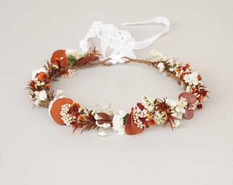 May include: A brown and white floral crown with dried flowers and leaves. The crown is tied with a white lace ribbon.