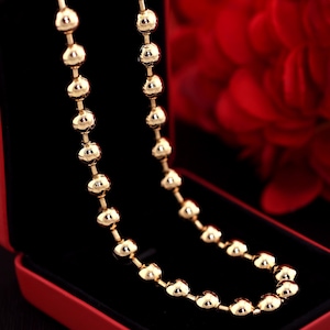 Op de afbeelding: Een gouden ketting met ronde kralen in een rode fluwelen juwelendoos.