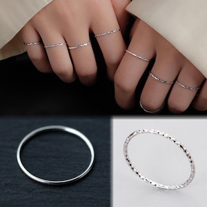 May include: A selection of silver rings, featuring both plain and patterned designs. The rings are shown on fingers and also displayed separately. The rings are delicate and appear to be made of a shiny metal.