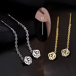 May include: A pair of rose-shaped dangle earrings with a delicate chain. One pair is silver and the other is gold.