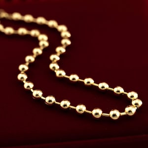 Peut inclure: Un collier en chaîne dorée avec des perles rondes. La chaîne est sur un fond de velours rouge.