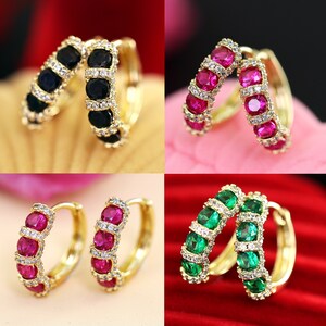 Peut inclure: Quatre paires de boucles d'oreilles créoles en or avec des pierres précieuses de différentes couleurs. Les boucles d'oreilles sont noires, rouges, vertes et roses.