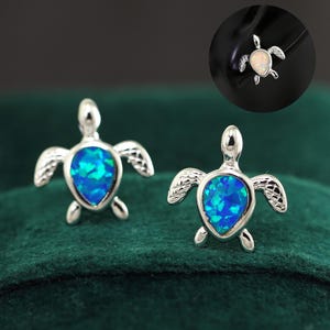 Puede incluir: Un par de pendientes de plata con forma de tortuga con piedras preciosas de ópalo azul. Los pendientes son pequeños y delicados, perfectos para el uso diario.
