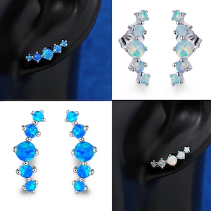 Puede incluir: Un par de pendientes de plata con un diseño curvo que presenta cinco piedras de ópalo azul. Los pendientes se muestran en la oreja de un maniquí.