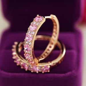 Puede incluir: Un par de pendientes de aro de oro con piedras de circonita cúbica rosas engastadas alrededor de los aros.