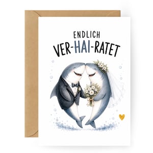 May include: A white greeting card featuring an illustration of two sharks in wedding attire. One shark wears a black tuxedo with a bowtie, and the other wears a floral crown and veil while holding a bouquet. The text reads ENDLICH VER-HAI-RATET.
