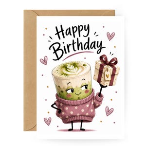 Könnte beinhalten: Geburtstagskarte mit einem Cartoon-Matcha-Latte-Charakter, der ein Geschenk hält. Der Charakter trägt einen rosa Pullover mit Punkten. Die Worte "Happy Birthday" stehen über der Figur. Die Karte befindet sich auf einem weißen Hintergrund mit Herzen.