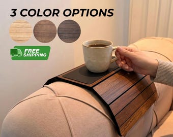 May include: A flexible wooden sofa arm tray with a dark brown finish and a black non-slip center panel. The tray is draped over a beige upholstered sofa arm, supporting a beige ceramic mug. Text reads 3 COLOR OPTIONS.