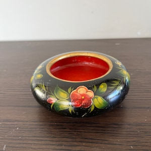 Peut inclure: Un petit bol en bois noir avec un intérieur rouge et des motifs floraux peints à la main. Le bol présente des fleurs rouges, vertes et jaunes avec des accents dorés.